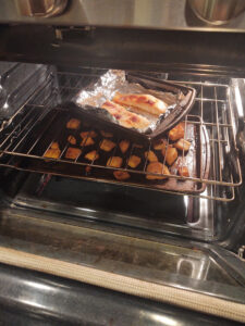Salmon in a pan in the oven with a baking sheet of butternut squash on the rack below it.