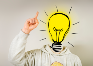 Photo of a man with his finger pointing upward and a lit lightbulb where his head should be.