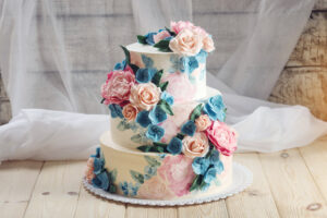 A three-tiered wedding cake decorated with pink roses and blue flowers.