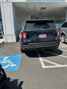 A vehicle half in and half out of a handicapped parking space.