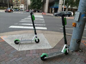 Two scooters parked near a curbcut; one totally blocking it and the other blocking some of it.