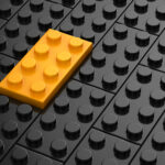 A bunch of black Lego pieces with one of the same size and shape yellow pieces all joined together.