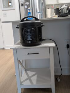 An Instant Pot on top of a white table and near an electric outlet.