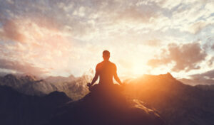 A person in a zen pose doing meditation at sunset on a mountain top.